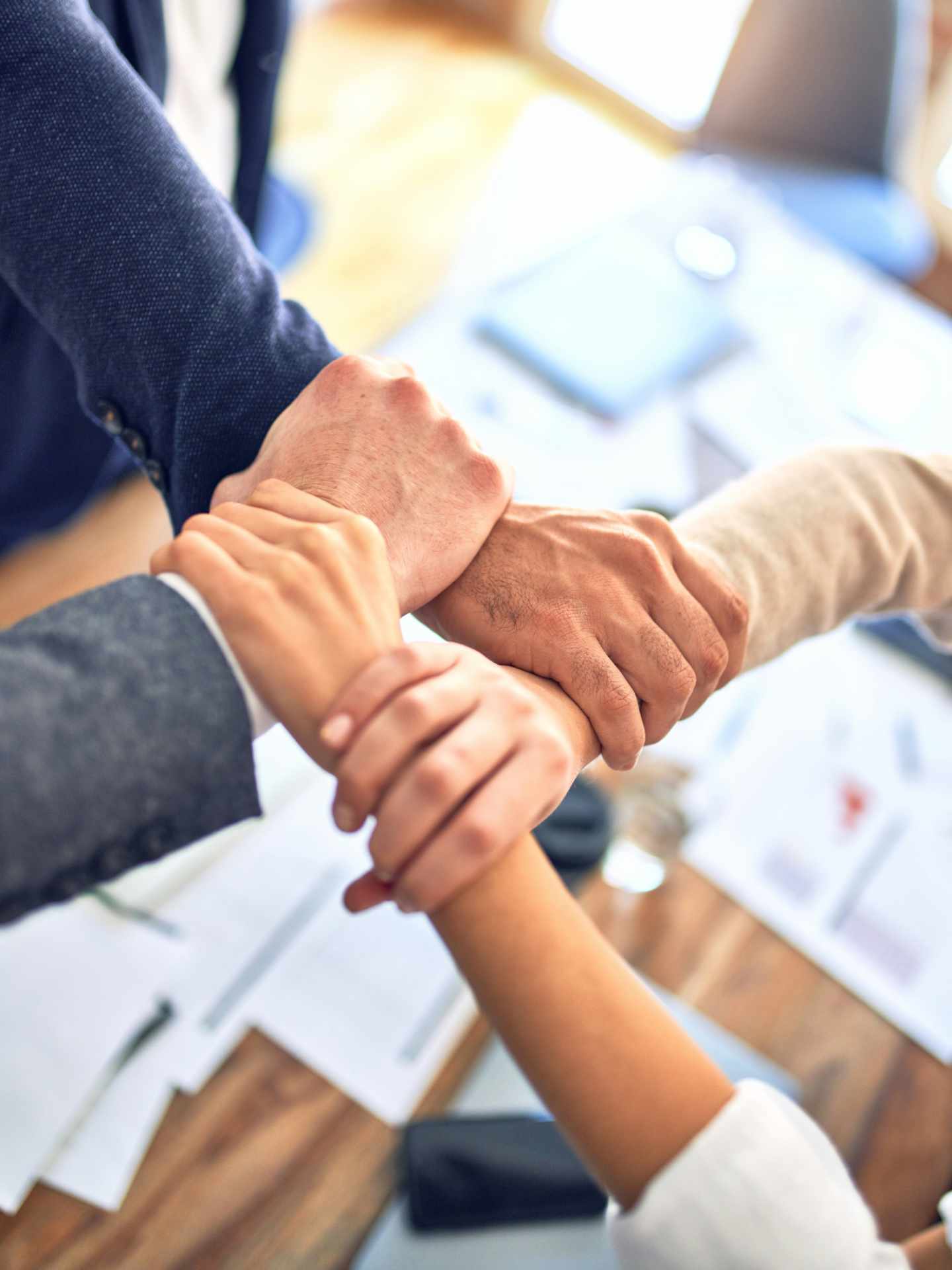 Vier Kolleg:innen unterschiedlicher Hautfarbe und Geschlechter halten sich gegenseitig an den Handgelenken fest.